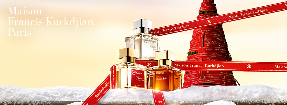 Drei elegante Parfumflakons von Maison Francis Kurkdjian Paris stehen auf verschneitem Untergrund vor einem stilisierten Weihnachtsbaum aus roten Geschenkbändern. Auf den goldenen und transparenten Flakons reflektiert warmes Licht, im Vordergrund liegt ein rotes Band mit dem Markenlogo. Text links: „Maison Francis Kurkdjian Paris“.