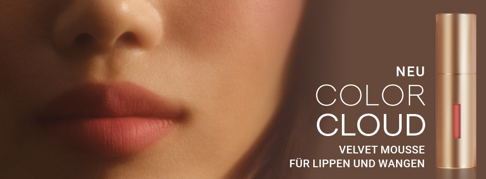 Nahaufnahme eines Gesichts mit weich geschminkten Lippen und zartem Rouge. Rechts daneben ein goldener Flakon des Produkts 'Color Cloud'. Text: 'NEU COLOR CLOUD – Velvet Mousse für Lippen und Wangen'.